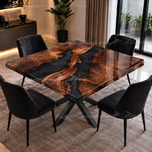 May include: A square dining table featuring a natural wood grain surface with a central black resin inlay, supported by a black metal X-shaped base, accompanied by four black upholstered chairs with thin black metal legs.