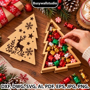 May include: A light-coloured wooden Christmas tree-shaped box with a removable lid featuring a laser-cut reindeer, stars, and snowflakes. The open base contains assorted red, green, silver, and gold wrapped sweets and peppermint swirls.