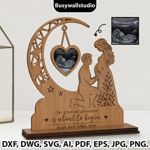 May include: A laser-cut wooden display featuring a crescent moon, a heart-shaped frame containing an ultrasound image, and silhouettes of a kneeling person and a pregnant person. The text reads: Our greatest adventure is about to begin. BABY DUE APRIL 2024.