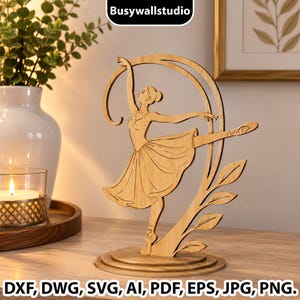 Op de afbeelding: Een lichtgekleurd houten uitgesneden sculptuur van een ballerina in een danshouding, met een zwierige rok en lintdetail, gemonteerd op een ronde voet. De tekst Busywallstudio staat bovenaan, en DXF, DWG, SVG, AI, PDF, EPS, JPG, PNG onderaan.