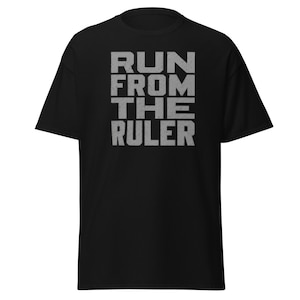 Puede incluir: Una camiseta negra de manga corta con el texto RUN FROM THE RULER impreso en una fuente de bloque gris claro con efecto desgastado en el centro del pecho. La prenda tiene un cuello redondo y una silueta de corte recto estándar.