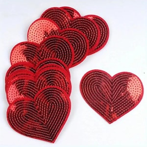 May include: A collection of heart-shaped patches covered in shiny red sequins. The patches are arranged in a stacked cluster with one separate heart-shaped patch positioned to the right, all featuring a distinct concentric circular pattern.