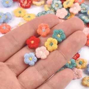 May include: A collection of small, multi-coloured embroidered flower patches in shades of red, orange, yellow, light blue, teal, and pale pink. Each individual flower features a contrasting centre colour and a textured, raised thread finish.