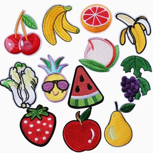 May include: A collection of twelve embroidered fabric patches featuring various fruits and vegetables, including cherries, bananas, a grapefruit slice, a peeled banana, bok choy, a pineapple with sunglasses, watermelon, grapes, strawberry, apple, and pear.