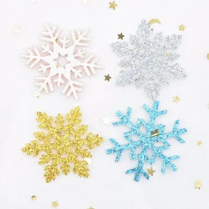 May include: Four decorative snowflake ornaments featuring glittery finishes in white, silver, gold, and light blue. Each snowflake displays a distinct geometric branch pattern, arranged in a grid formation against a plain white background.