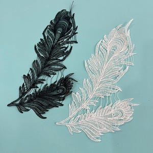 May include: Two pairs of embroidered lace appliqués shaped like peacock feathers. One pair is black and the other is white. Each appliqué features intricate thread work detailing the central eye and the fine, branching barbs of a feather.
