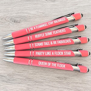 May include: Five coral pink retractable ballpoint pens with silver accents and black stylus tips. Each pen features white text: BE A FLAMINGO, STAY BALANCED; RUFFLE SOME FEATHERS; STAND TALL & BE FABULOUS; PARTY LIKE A FLOCK STAR; QUEEN OF THE FLOCK.