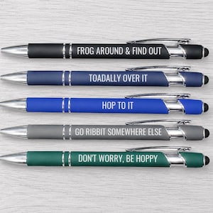May include: A set of five retractable ballpoint pens with stylus tips, featuring silver accents and white text. The pens are black, navy, blue, gray, and green, with the phrases: FROG AROUND & FIND OUT, TOADALLY OVER IT, HOP TO IT, GO RIBBIT SOMEWHERE ELSE, and DON'T WORRY, BE HOPPY.