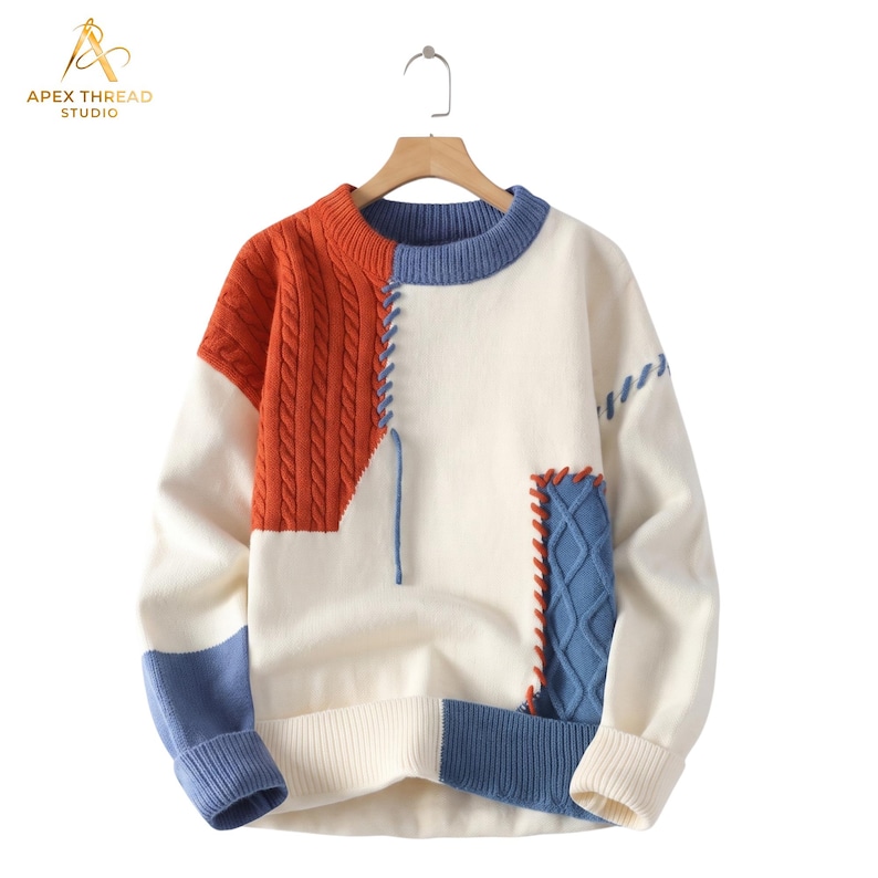 May include: A long-sleeve crewneck sweater featuring a color-blocked design in cream, burnt orange, and blue. The garment includes cable-knit panels, ribbed cuffs and hem, and decorative whipstitch detailing connecting the contrasting fabric sections.