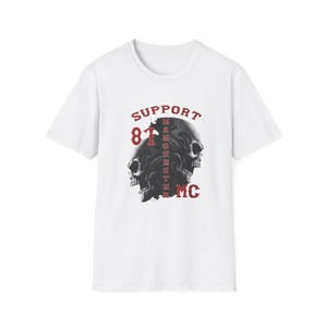 May include: A white short-sleeved t-shirt featuring a graphic print of two dark skulls. The text "SUPPORT 81 MC" is printed in red, with the word "MANCHESTER" written vertically in red between the skulls. The design is centered on the chest.
