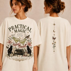 May include: An off-white t-shirt featuring a front graphic with the text Practical Magic, two margarita glasses, black cats, books, and flowers. The back graphic displays a vertical design with a star, moon, butterfly, and floral elements.