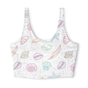 May include: A white sleeveless crop top featuring a repeating pattern of various seashells and starfish in soft pastel shades of pink, purple, blue, and orange, accented with small scattered blue dots across the entire garment surface.