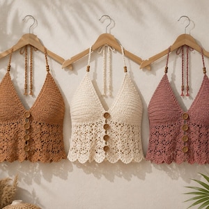 Può includere: Tre top all'americana in uncinetto nei colori ruggine, crema e rosa antico. Ogni top presenta un profondo scollo a V, un'abbottonatura frontale con quattro bottoni in legno, un orlo smerlato e sottili spalline intrecciate con perline.