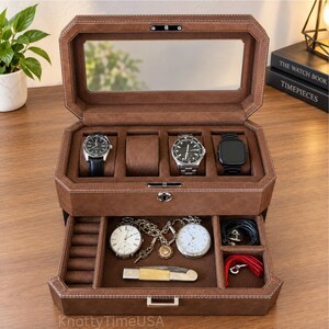 May include: A brown leather watch box with a glass lid, featuring four upper compartments with three watches and one empty cushion, and a lower pull-out drawer containing two pocket watches, a folding knife, and small accessories.