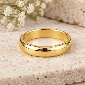 Könnte beinhalten: Ein polierter Goldring mit einer glatten, abgerundeten Oberfläche und einem reflektierenden Finish. Der Ring ist kreisförmig mit gleichbleibender Breite und zeigt einen hellen Gelbgoldton, der das Licht auf seiner gewölbten Außenfläche einfängt.