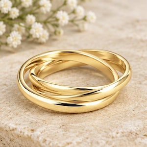 May include: A polished gold ring composed of three interlocking bands that create a continuous, fluid circular shape. The metal surface is smooth and reflective, showcasing a bright yellow gold tone throughout the entire structure of the ring.