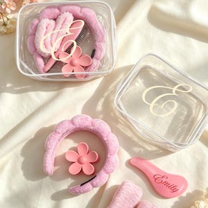 Peut inclure: Une pochette rectangulaire transparente avec une lettre E blanche, contenant un bandeau rose pelucheux, une pince à cheveux fleur rose et une brosse à cheveux rose marquée Emily. À l'extérieur, un bandeau rose, une pince fleur, deux bracelets éponges roses et une brosse rose avec le nom Emily.