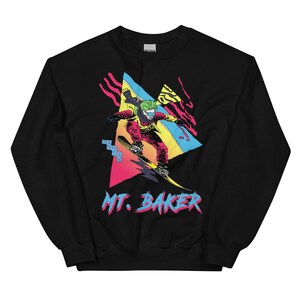 May include: Black sweatshirt featuring a retro-style graphic of a person snowboarding down a mountain. The graphic is in bright colours, including pink, blue, yellow, and green. The text "MT. BAKER" is printed below the graphic.