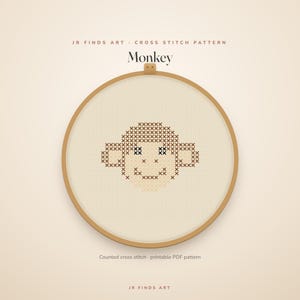 May include: A circular wooden embroidery hoop containing a cross stitch pattern of a monkey face. The design features brown and black thread on a light fabric. Text at the top reads JR FINDS ART CROSS STITCH PATTERN Monkey, and at the bottom, Counted cross stitch printable PDF pattern JR FINDS ART.