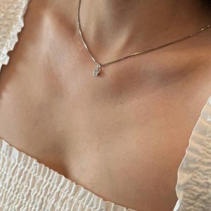 Op de afbeelding: Een zilverkleurige ketting met een kleine, vijfpuntige sterhanger. De sterhanger is in het midden versierd met een enkele, heldere, fonkelende steen. De ketting rust op het sleutelbeen en heeft een verfijnd schakelontwerp.