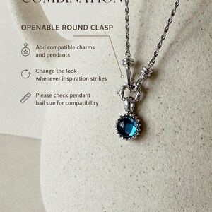 Pode incluir: Um colar de corrente de corda prateada com um fecho redondo que pode ser aberto e um pingente circular com uma pedra azul profunda. O texto diz: CREATE YOUR OWN COMBINATION, OPENABLE ROUND CLASP, Add compatible charms and pendants, Change the look whenever inspiration strikes, Please check pendant bail size for compatibility.