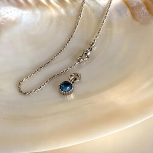 Pode incluir: Um colar de corrente de corda prateada com um pequeno pendente redondo que apresenta uma pedra caboch&atilde;o azul profunda e lisa, engastada numa moldura de metal estriado. O colar inclui um fecho de lagosta e um pequeno anel de liga&ccedil;&atilde;o.