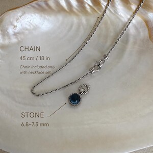Pode incluir: Um colar de corrente torcida prateada com 45 cm de comprimento e um pendente circular com uma pedra azul-escura de 6,8&ndash;7,3 mm. A corrente inclui um fecho decorativo e &eacute; apresentada com um pendente a condizer neste conjunto.