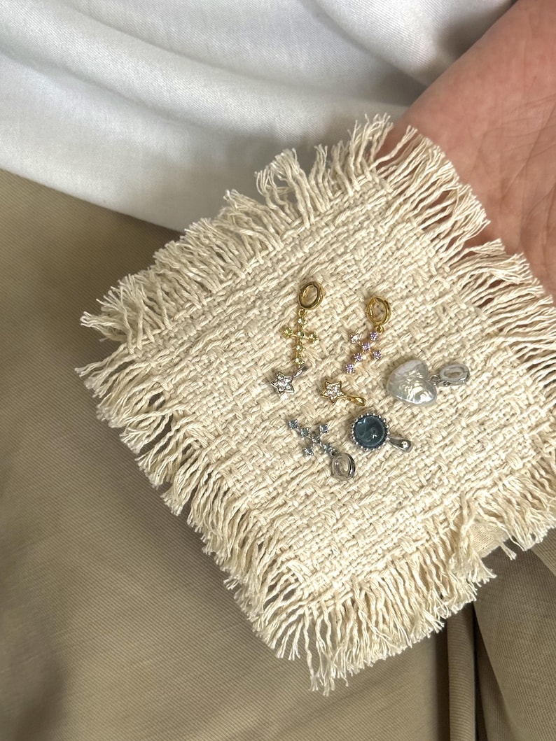 Pode incluir: Uma cole&ccedil;&atilde;o de seis pequenos pingentes de metal, incluindo dois pingentes em forma de cruz com pedras transparentes, um pingente de estrela, um pingente de cora&ccedil;&atilde;o, um pingente circular com centro azul e uma cruz com pedras violeta claro.