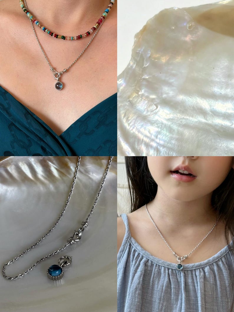 Pode incluir: Um colar de corrente de corda prateada com um pingente de pedra preciosa redonda de tom azul e uma arma&ccedil;&atilde;o de metal texturizado. O colar inclui um fecho de alavanca e &eacute; exibido sobreposto a um colar de contas multicolorido.