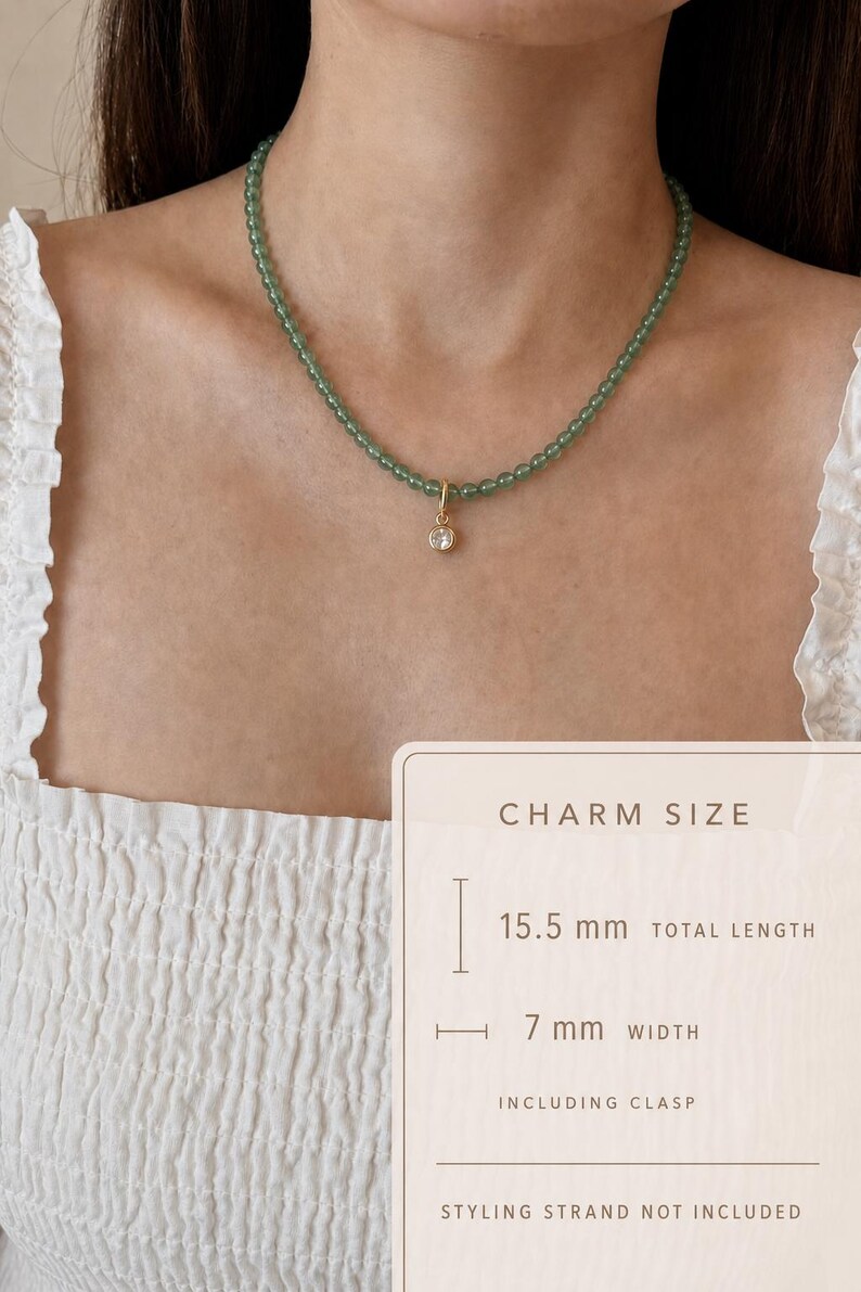 Puede incluir: Un collar con peque&ntilde;as cuentas redondas de color verde transl&uacute;cido y un dije dorado con una piedra redonda transparente. Una superposici&oacute;n indica que el dije mide 15,5 mm de largo total y 7 mm de ancho, incluyendo el cierre.