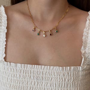 Puede incluir: Un collar de cadena en tono dorado que presenta una serie de peque&ntilde;os dijes circulares colgantes. Cada dije est&aacute; engastado con una sola piedra preciosa de colores vibrantes, incluyendo verde, transparente y rojo oscuro, suspendido de una cadena de eslabones rectangulares.