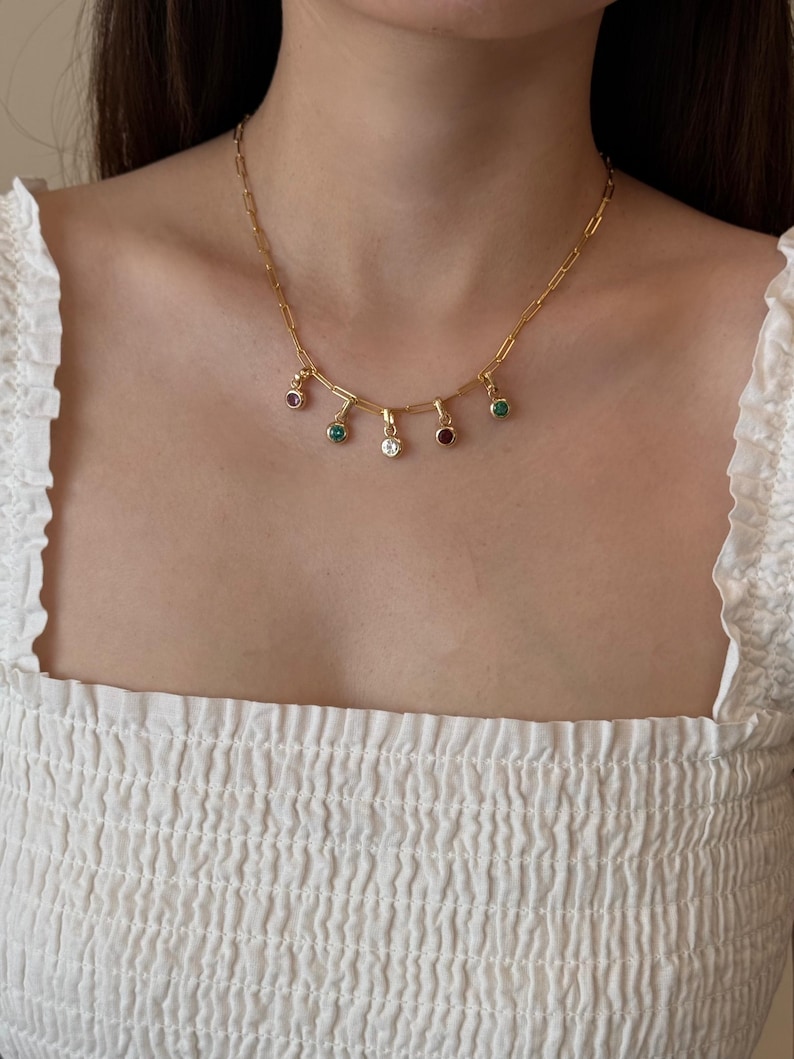 Puede incluir: Un collar de cadena en tono dorado que presenta una serie de peque&ntilde;os dijes circulares colgantes. Cada dije est&aacute; engastado con una sola piedra preciosa de colores vibrantes, incluyendo verde, transparente y rojo oscuro, suspendido de una cadena de eslabones rectangulares.