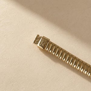 May include: A gold-toned metal bracelet with a ribbed, flexible link design. The clasp is clearly engraved with the text A9925 ITALY, indicating the origin and composition of the piece. The bracelet features a polished finish throughout.
