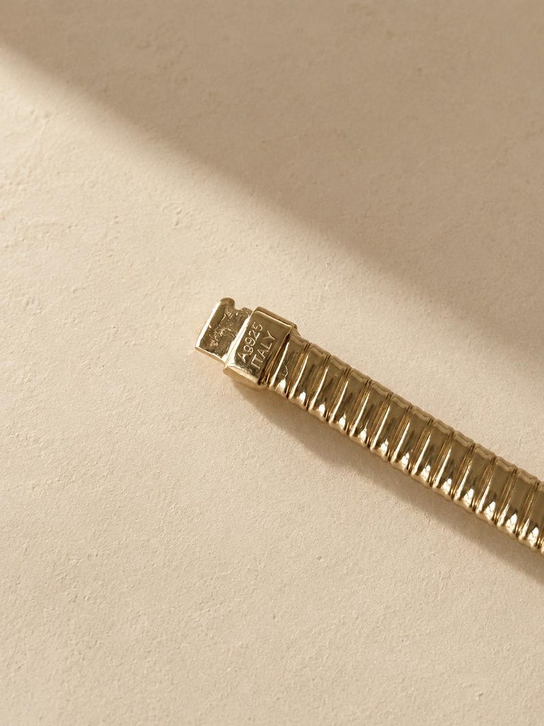 May include: A gold-toned metal bracelet with a ribbed, flexible link design. The clasp is clearly engraved with the text A9925 ITALY, indicating the origin and composition of the piece. The bracelet features a polished finish throughout.