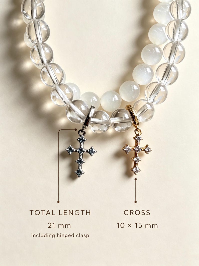 Puede incluir: Pulsera de cuentas esf&eacute;ricas transparentes y blancas con dos colgantes de cruz. Una cruz plateada y otra dorada, ambas con peque&ntilde;as piedras. El texto indica una longitud total de 21 mm incluyendo el cierre y un tama&ntilde;o de cruz de 10 x 15 mm.
