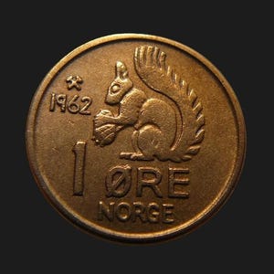 以下が含まれることがあります： 1962年製のブロンズ色のノルウェーの1オーレ硬貨。硬貨には、木の実を持つリスのレリーフ、1962という年号、小さなハンマーとツルハシのシンボル、数字の1、ØREという文字、そして浮き彫りになったNORGEという単語がデザインされています。