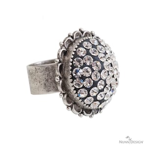 May include: A silver ring with a large, round, black stone set with clear rhinestones. The ring has a decorative, scalloped edge.