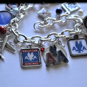 Puede incluir: Un brazalete de plata con varios abalorios, incluyendo un avi&oacute;n peque&ntilde;o, un abalorio cuadrado con el logotipo de American Airlines y un abalorio redondo con las letras "AA" en rojo, blanco y azul. El brazalete tambi&eacute;n tiene varias cuentas rojas y azules.