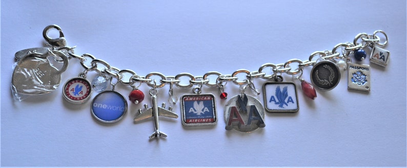 Puede incluir: Un brazalete de plata con varios dijes, incluyendo un avi&oacute;n de plata, un dije rojo y azul con las palabras "American Airlines", un dije de plata con las palabras "oneworld" y un dije de plata con las palabras "AA".
