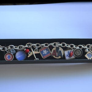 Puede incluir: Un brazalete de plata con varios dijes, incluyendo un coraz&oacute;n, un avi&oacute;n, un pasaporte y varios dijes con el logotipo de American Airlines. El brazalete est&aacute; en una caja negra.