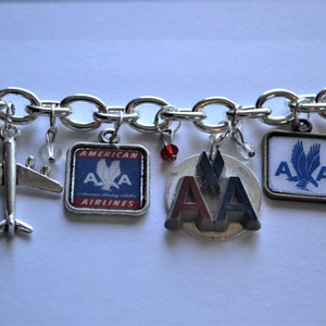 Puede incluir: Un brazalete de plata con varios dijes, incluyendo un avi&oacute;n peque&ntilde;o, un dije con el logotipo de American Airlines en rojo y azul, y un dije con el logotipo de American Airlines en rojo y azul con un &aacute;guila plateada.