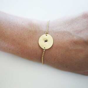 May include: A gold chain bracelet with a round gold charm featuring the letter "A" engraved on it.