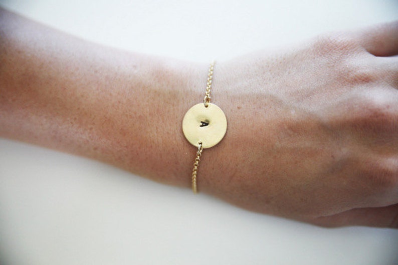 May include: A gold chain bracelet with a round gold charm featuring the letter "A" engraved on it.