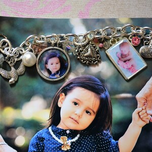 Könnte beinhalten: Ein silbernes Armband mit verschiedenen Charms, darunter ein kleiner Vogel, eine Perle, ein Herz und zwei Foto-Anhänger. Die Foto-Anhänger zeigen ein junges Mädchen und ein Baby. Das Armband hat auch einen Anhänger mit dem Text "Special Grandma".