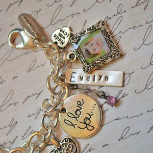 May include: Silver charm bracelet with various charms, including a heart, a circle with the text "I love you...", a small picture frame with a child's photo, a charm with the text "Made with love", and a charm with the name "Evelyn".