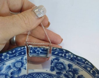 May include: A silver chain necklace with a rectangular pendant made from a piece of broken blue and white china. The pendant is framed in silver and has a floral design.