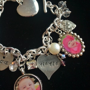 Peut inclure: Un bracelet à breloques en argent avec divers breloques, dont des cœurs, une perle, un cristal et deux breloques photo. Un breloque photo représente une petite fille portant un chapeau rose, et l'autre breloque photo représente une petite fille avec un grand sourire. Le breloque en forme de cœur dit "Yia Yia".