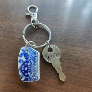 May include: A silver key chain with a blue and white ceramic charm and a silver key with the date 09.27.23 engraved on it.