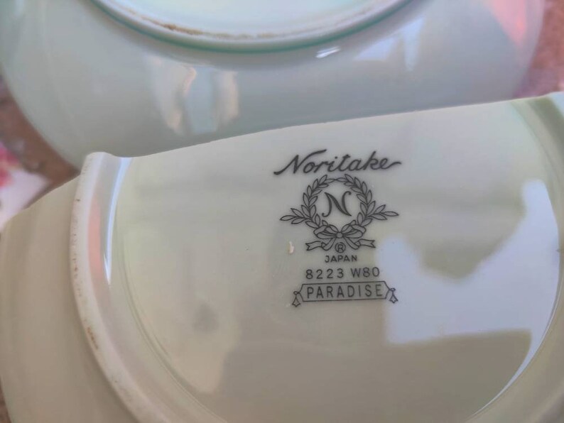 May include: A white porcelain saucer with a Noritake Japan logo and the words "8223 W80 Paradise".