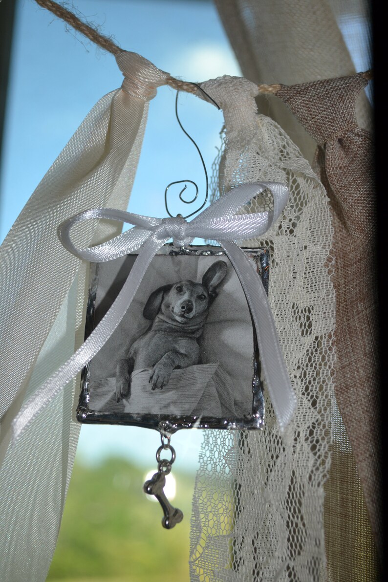 May include: A silver picture frame with a black and white photo of a dachshund dog. The frame is hanging from a white ribbon and has a silver bone charm.